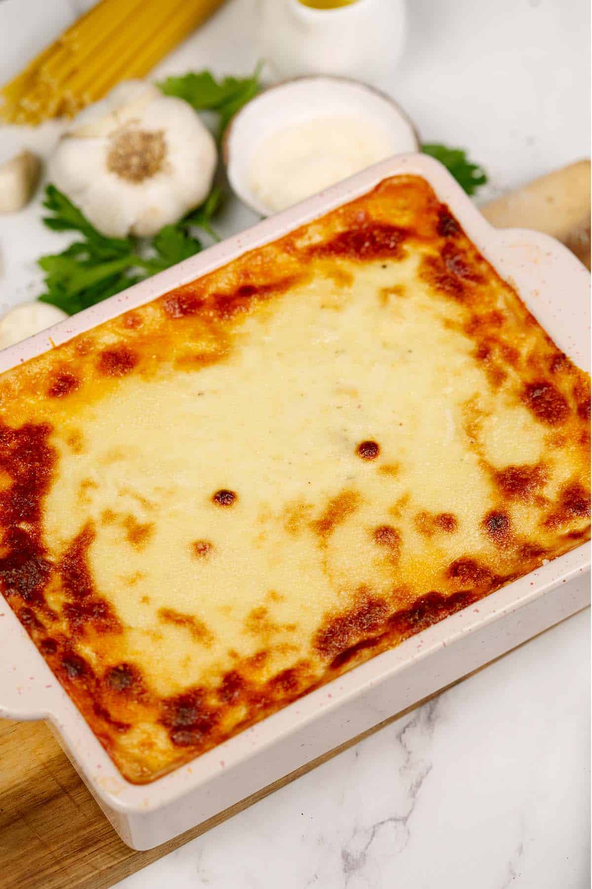 baking dish of pastitsio greek beef pasta bake on a table surrounded by extra ingredients