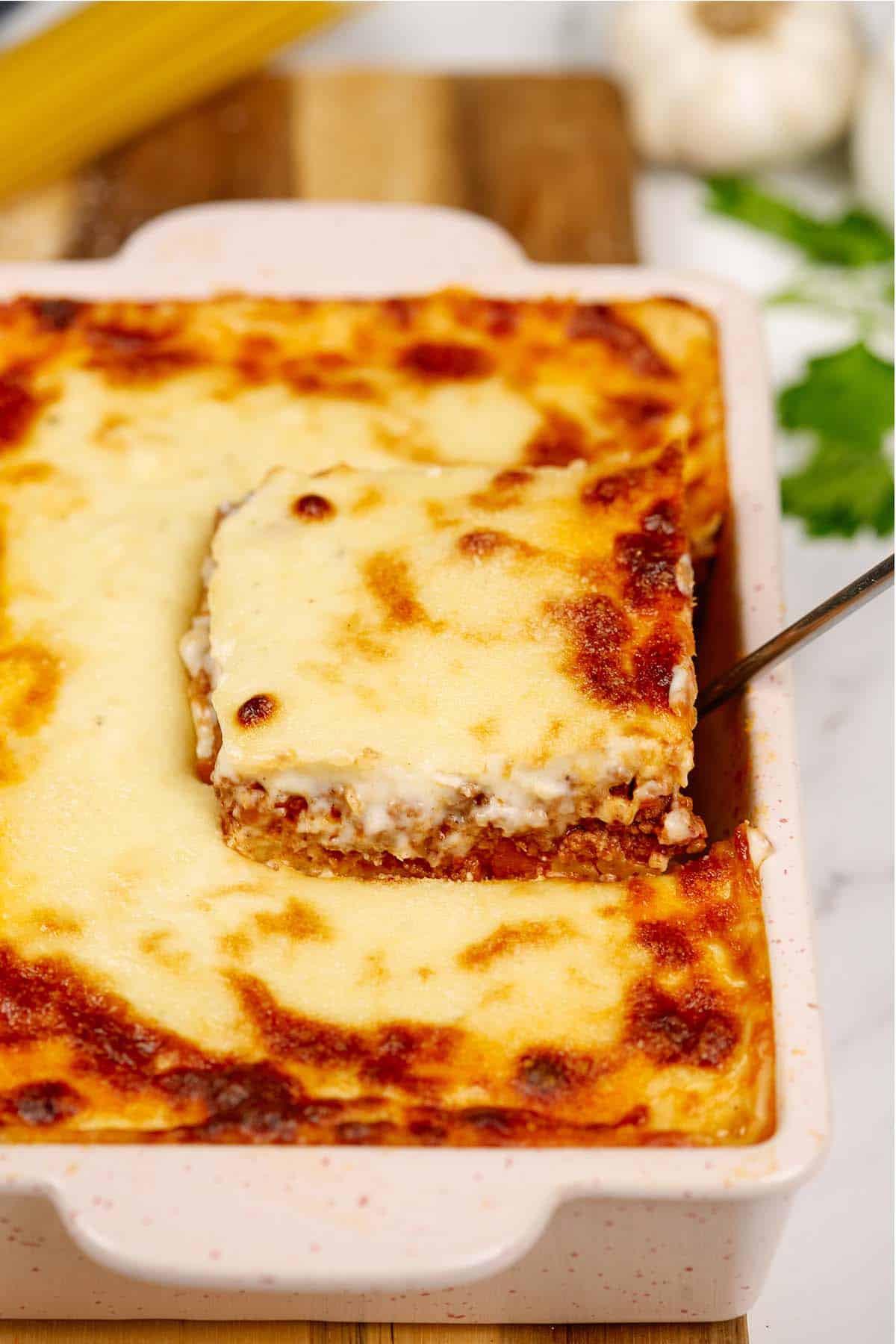 serving of pastitsio greek beef pasta bake being lifted from a baking dish with a spatula