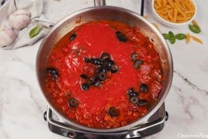 sauteeing olives, tomato sauce and other ingredients to make pepperoni pasta bake