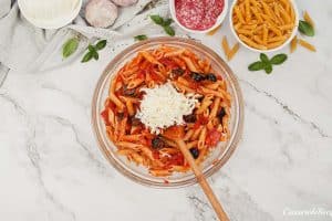 cheese being added to other ingredients to make pepperoni pasta bake