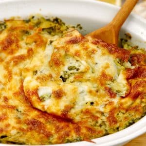 spoon scooping up a serving of spinach and artichoke pasta bake in a casserole dish