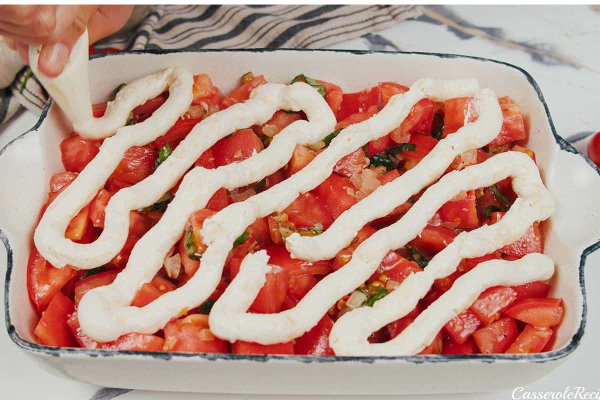 adding topping over the other ingredients to make a tomato casserole