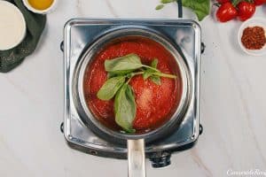 cooking basil with sauce to make Zucchini Parmesan