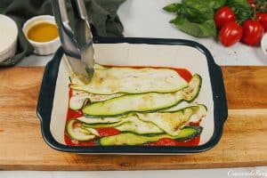 sliced zucchini being layered with sauce to make Zucchini Parmesan