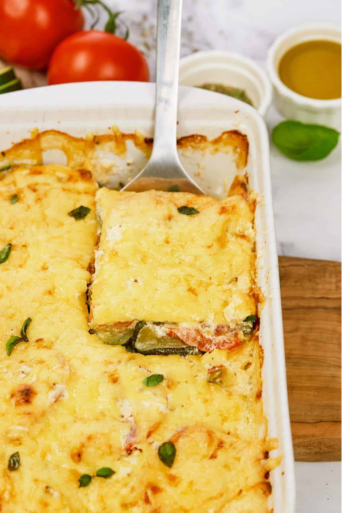spatula lifting a serving of zucchini tomato casserole from a baking dish to serve