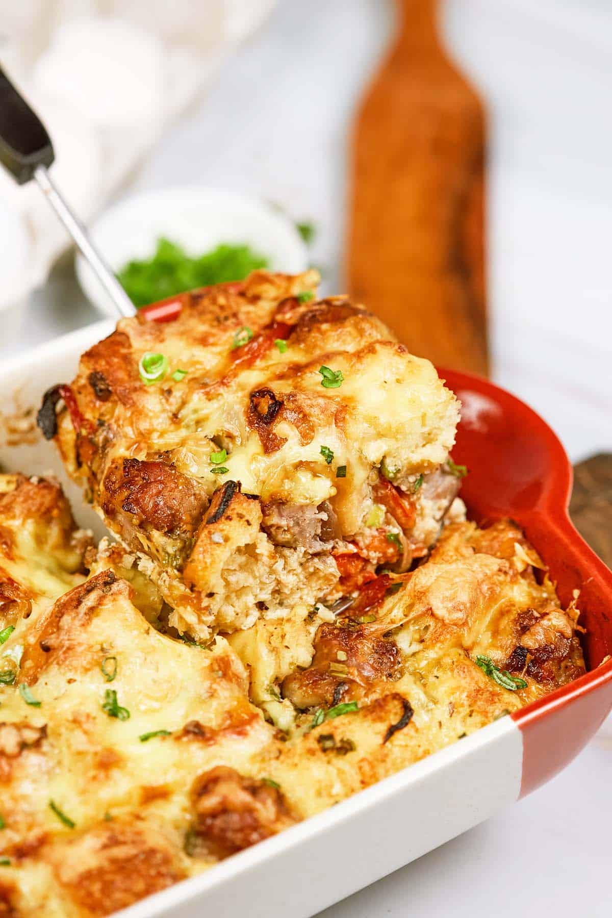 spoon lifting a serving of Cheesy Sausage Breakfast Casserole from a baking dish