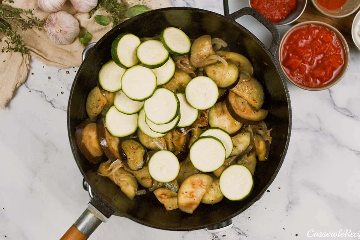 adding sliced zucchini to a casserole dish to make Tomato and Houllimi Bake