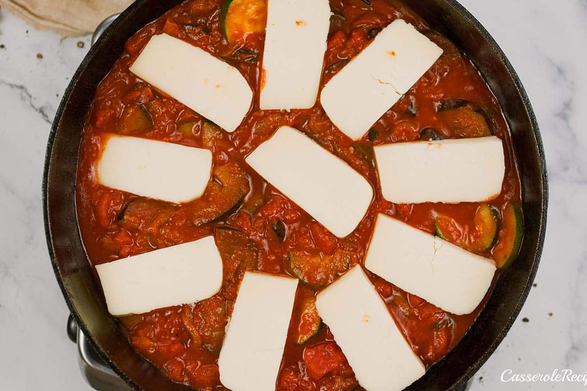 final step of topping the casserole with cheese prior to baking to make Tomato and Houllimi Bake