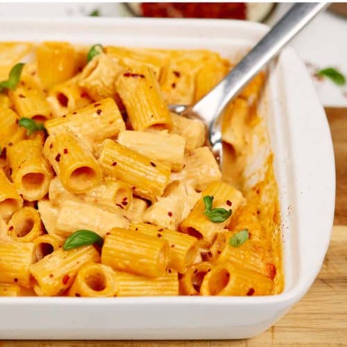 spoon scooping up a serving of baked feta pasta from a baking dish