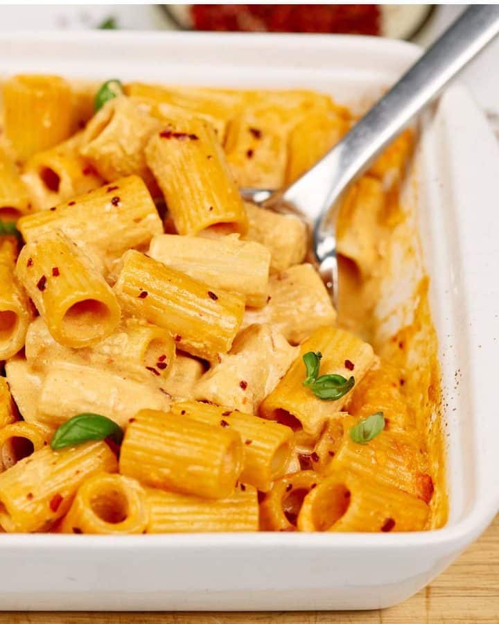 spoon scooping up a serving of baked feta pasta from a baking dish