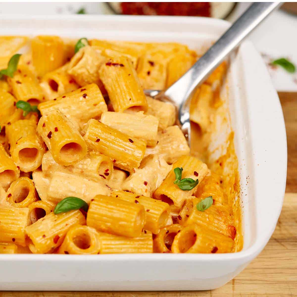 spoon scooping up a serving of baked feta pasta from a baking dish