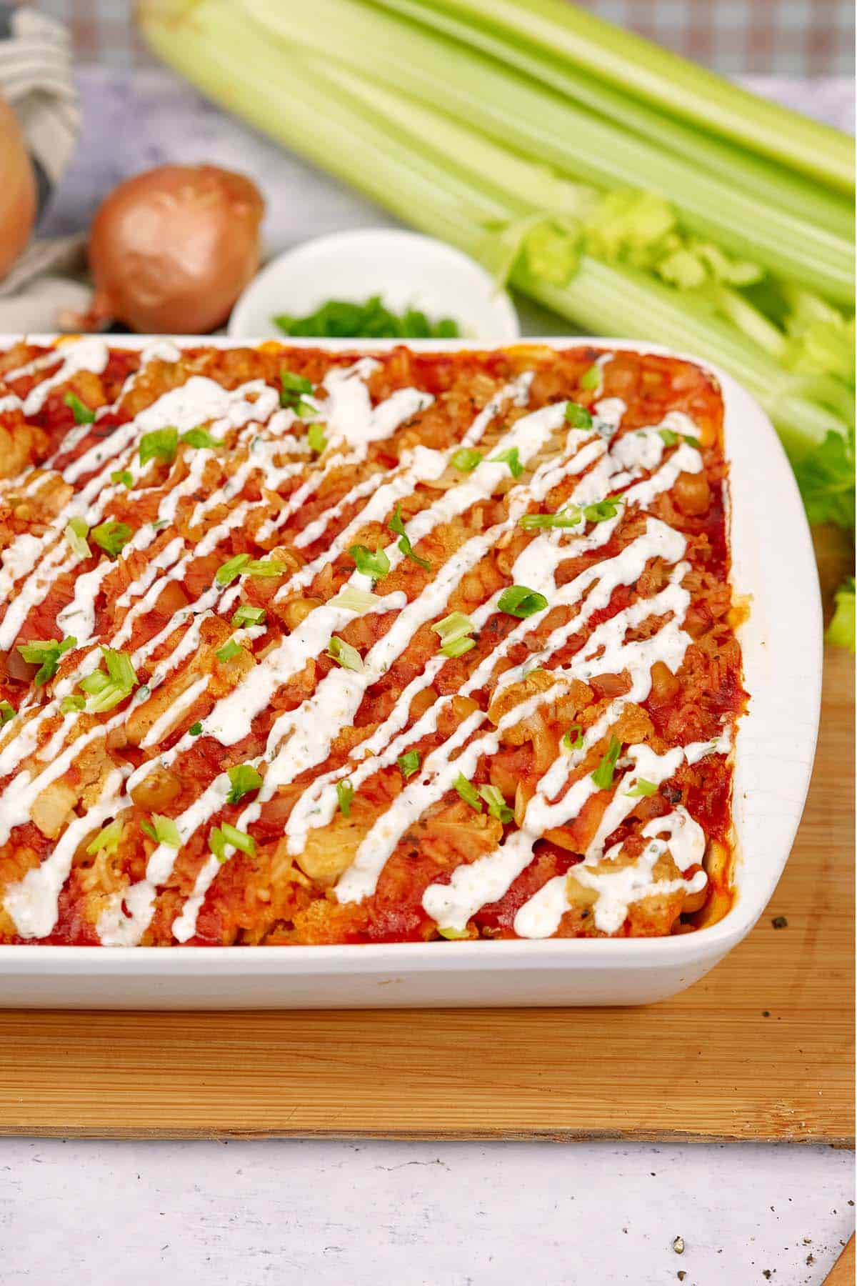 baking dish of buffalo cauliflower and chickpea casserole on a table with extra ingredients