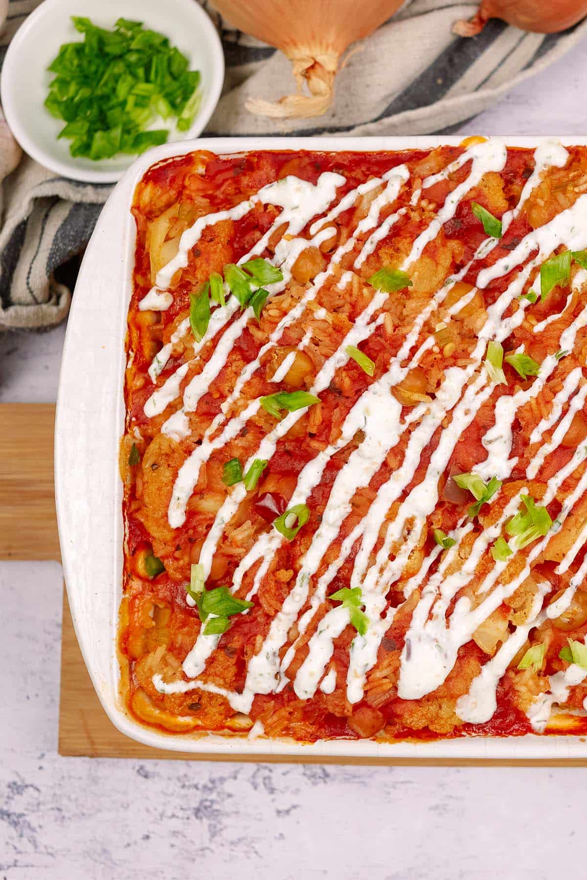 casserole dish of buffalo cauliflower and chickpea casserole on a table with extra ingredients