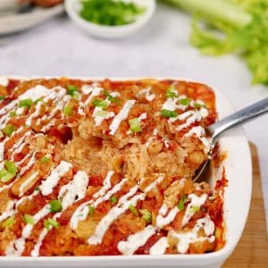 spoon scooping out a serving of buffalo cauliflower and chickpea casserole from a baking dish