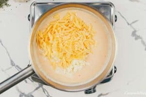 cheese being added to cream sauce to make creamy cauliflower casserole