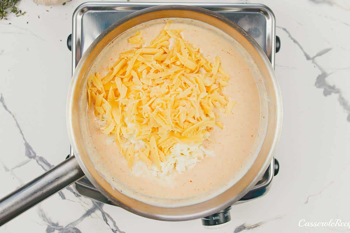 cheese being added to cream sauce to make creamy cauliflower casserole