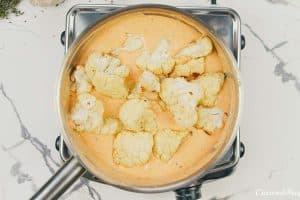 cauliflower florets being combined with sauce to make creamy cauliflower casserole