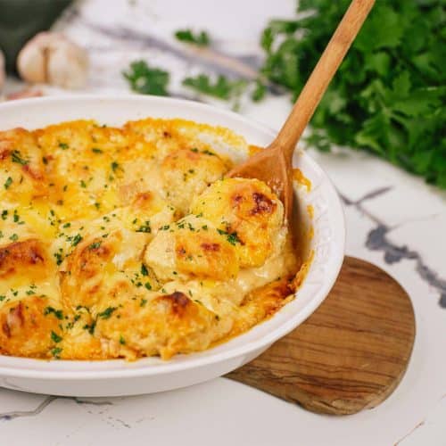 spoon scooping out a serving of creamy cauliflower casserole from a baking dish