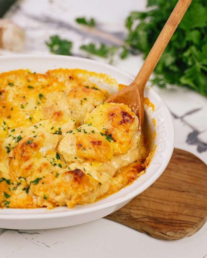 spoon scooping out a serving of creamy cauliflower casserole from a baking dish