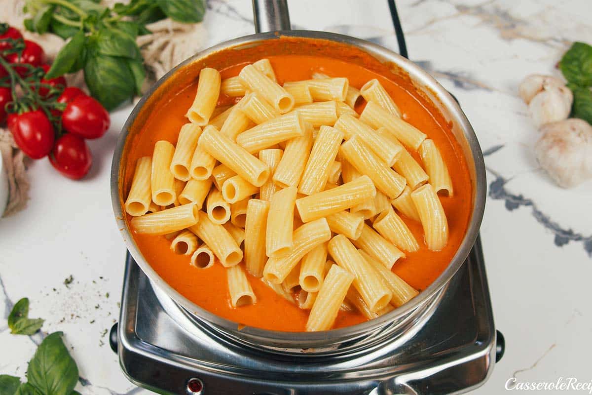 adding pasta to mixture to make creamy sun-dried tomato and roasted red pepper casserole