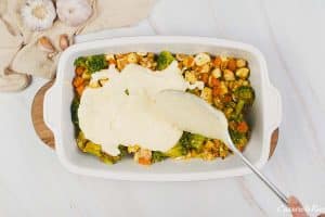 spooning batter on top of veggies to make curried chicken and grits casserole