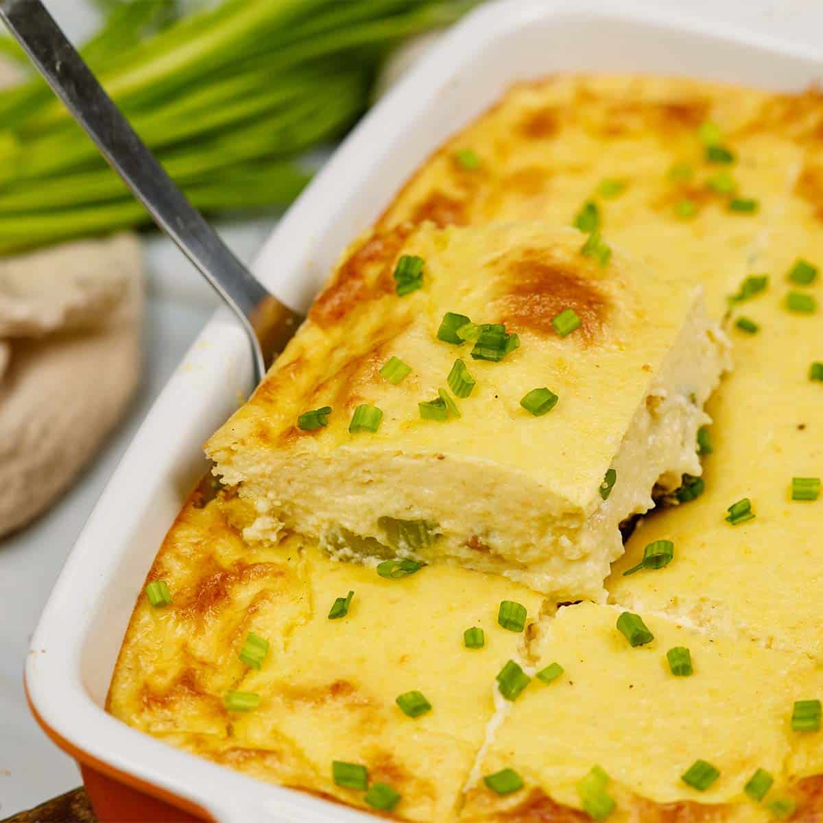 spatula lifting a serving of curried chicken and grits casserole from a baking dish