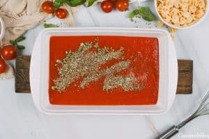 sauce and herbs in a baking dish to make dump and go meatball lasagna