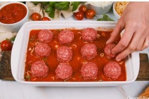 layering sauce and uncooked meatballs in a baking dish to make dump and go meatball lasagna