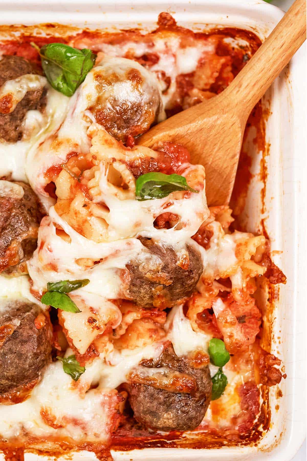 closeup of a spoon scooping a serving of dump and go meatball lasagna from a baking dish