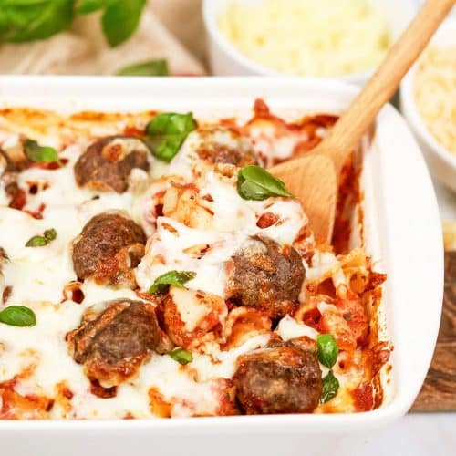 spoon scooping up a serving of dump and go meatball lasagna from a baking dish