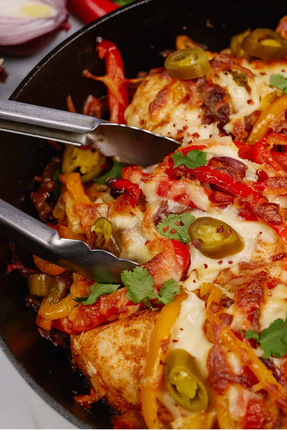 tongs lifting a serving of fajita chicken bake from a casserole dish