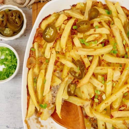 overhead view of baking dish filled with french fry casserole on a table with extra ingredients