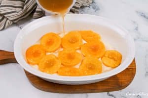 pouring sauce over fresh peaches to make peach, almond and caramel self-saucing pudding