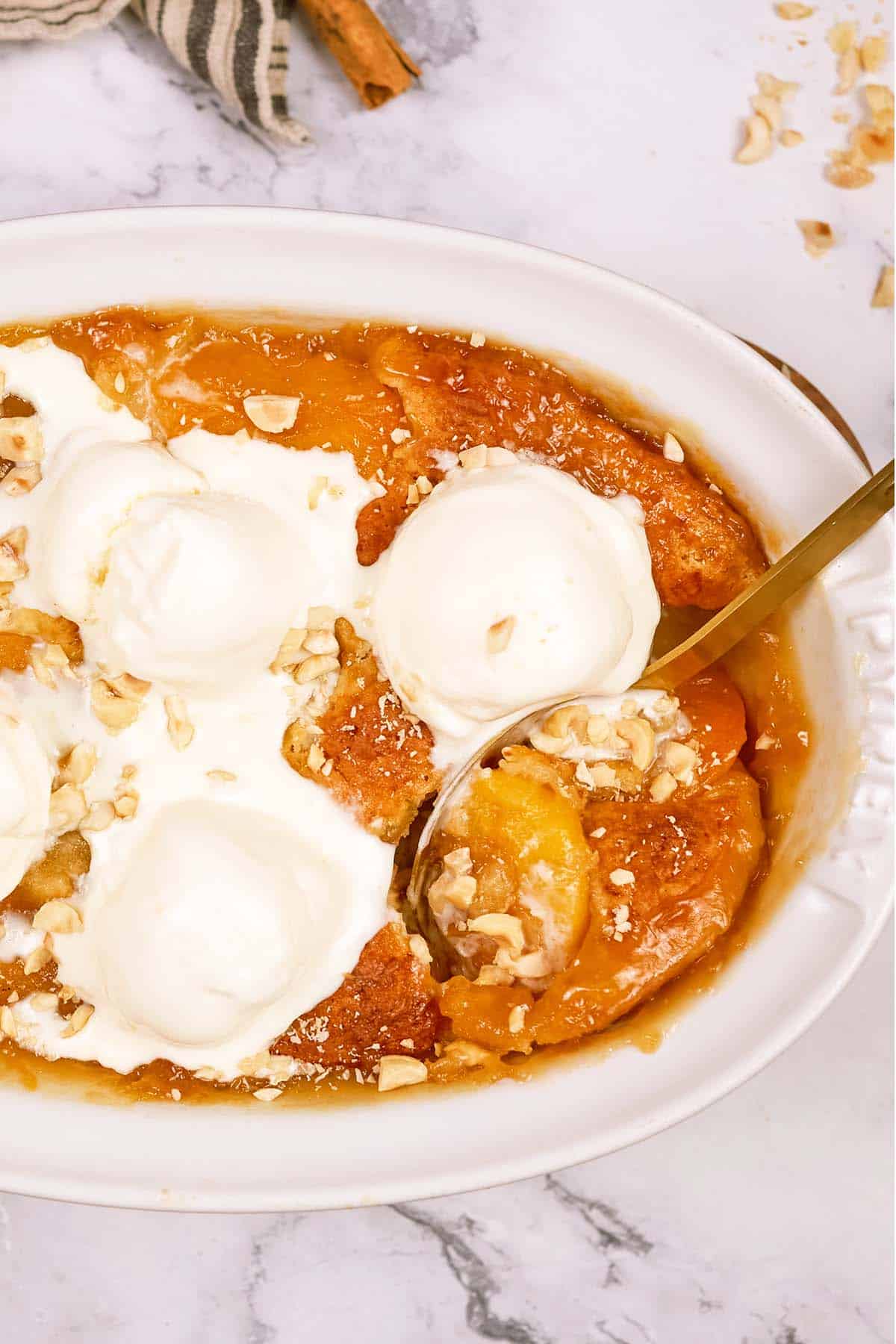 spoon scooping up a serving of peach, almond and caramel self-saucing pudding from a baking dish