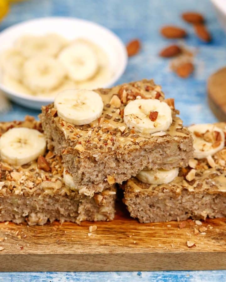 squares of peanut butter banana baked oatmeal on a serving board with other ingredients surrounding