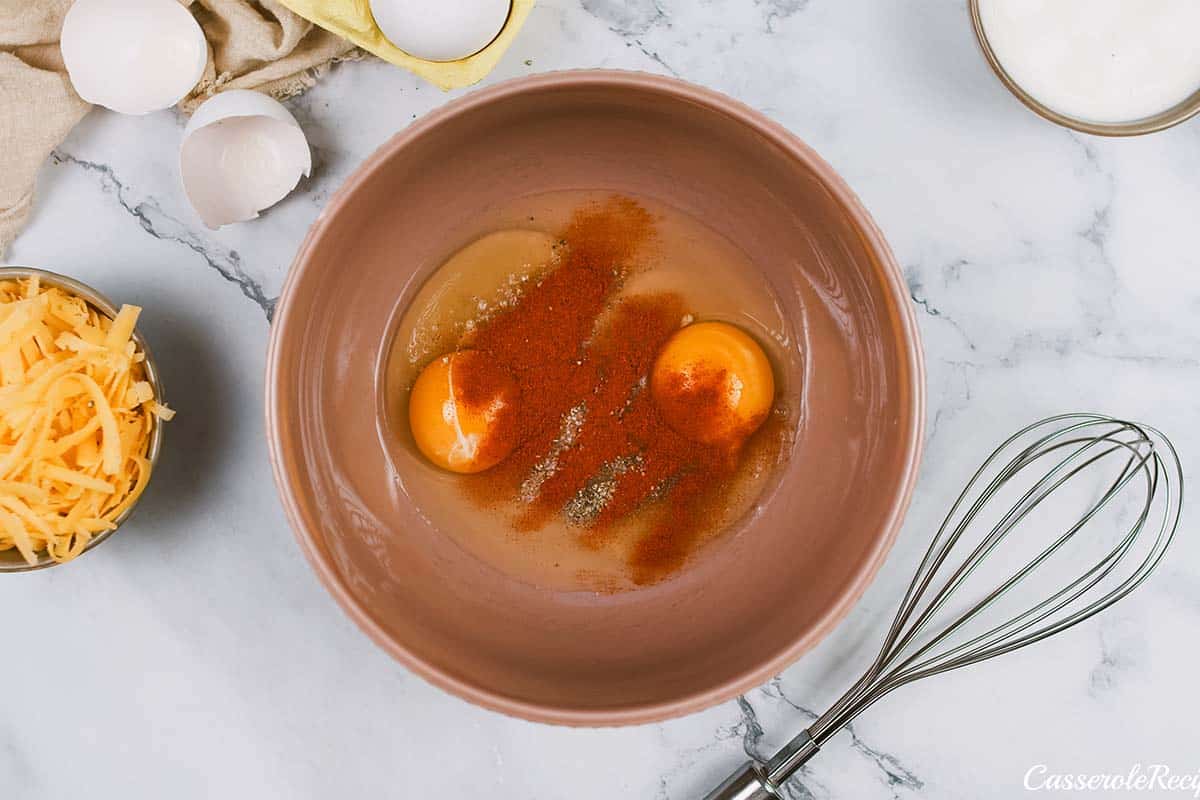 adding spices to eggs for a sauce for pigs in a blanket breakfast casserole