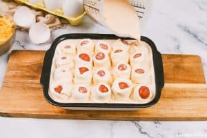 adding sauce into baking dish of pigs in a blanket breakfast casserole