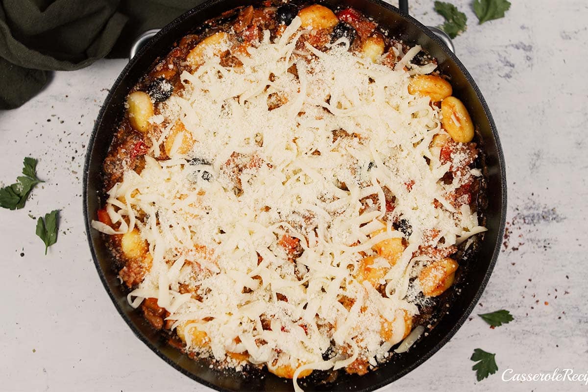 covering a casserole dish of supreme pizza gnocchi with cheese before baking