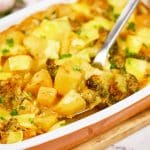 spoon scooping up a serving of vegan potato broccoli casserole from a baking dish