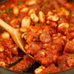 closeup of a spoon lifting a serving of vegan sausage casserole from a baking dish