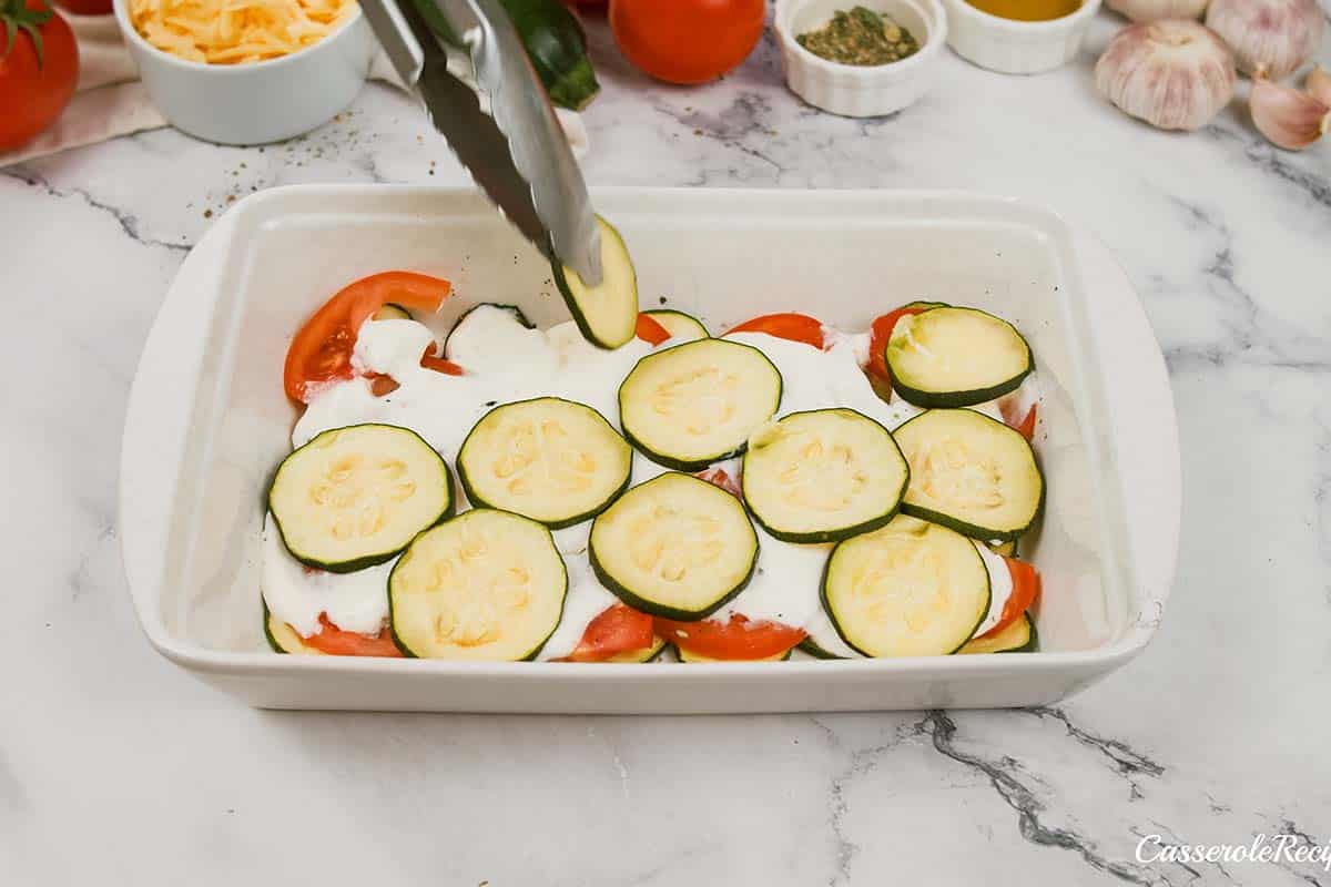 layering zucchini and tomatoes in a baking dish to make zucchini tomato casserole