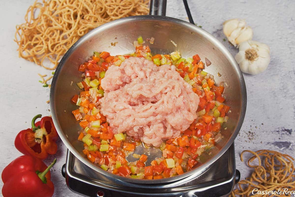 adding meat to a pan with vegetables to make Chicken chow mein casserole