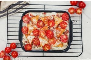 final step of making alfredo bacon tot casserole by topping with tomatoes before baking