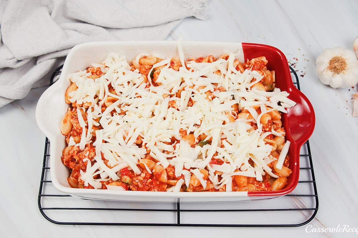 final step of making baked cavatelli casserole by topping with shredded cheese prior to baking