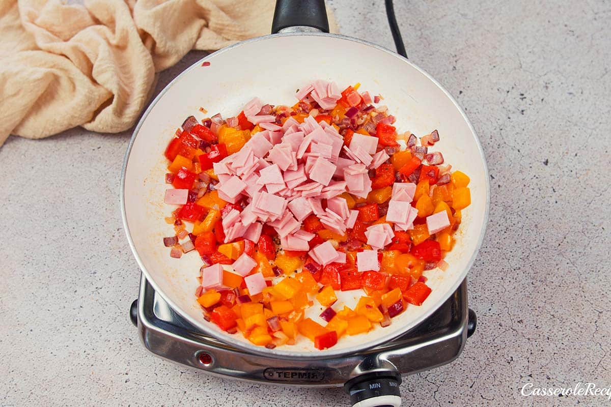 ham being added to cooked vegetables to make a baked denver omelette