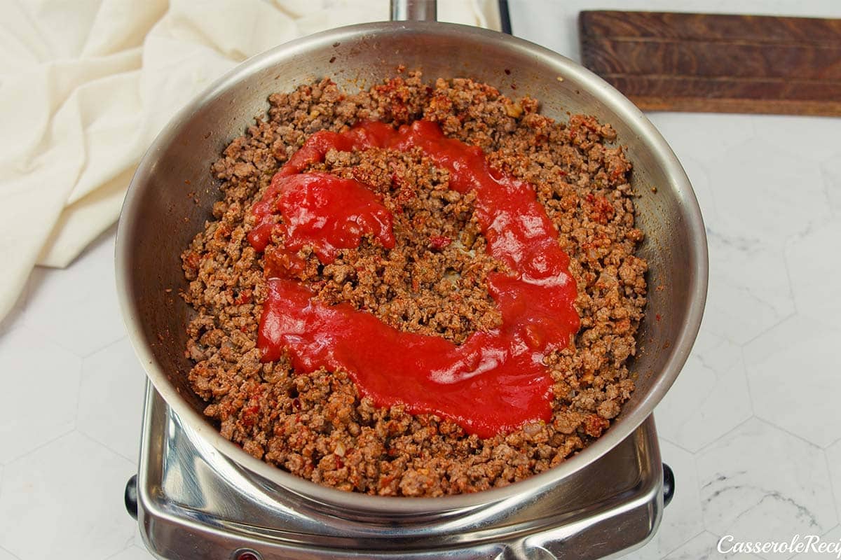 tomato sauce being added to meat to make cheeseburger casserole