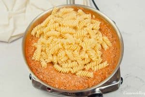 noodles being added to the mixture of other ingredients to make cheeseburger casserole