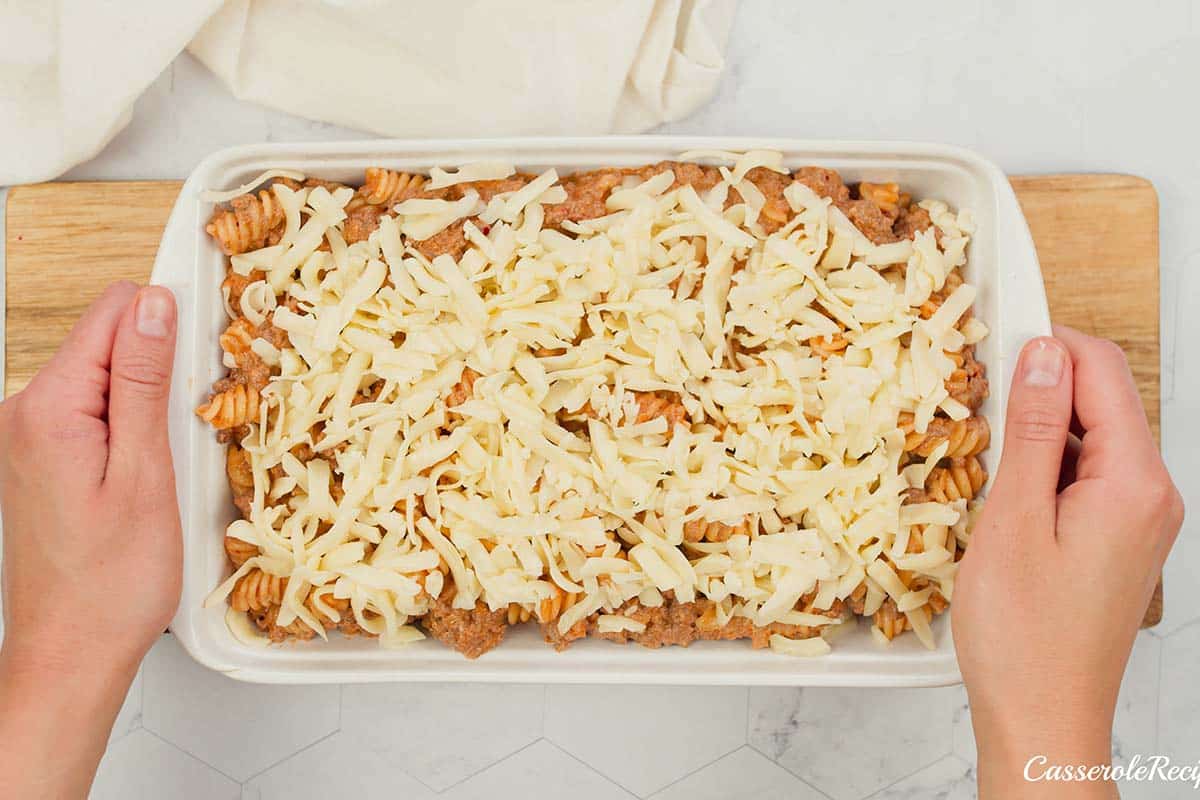 final step of making cheeseburger casserole by topping with cheese prior to baking