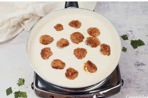 adding meatballs to cream sauce to make creamy meatball casserole