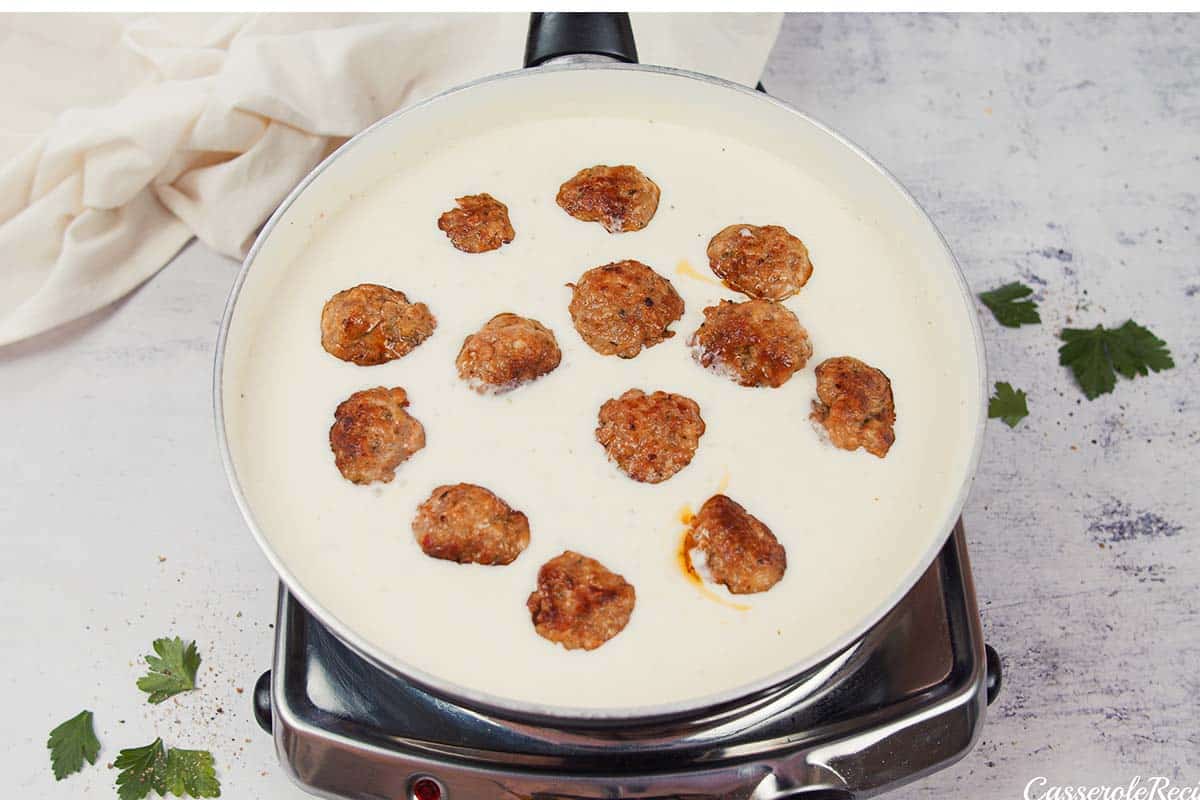 adding meatballs to cream sauce to make creamy meatball casserole